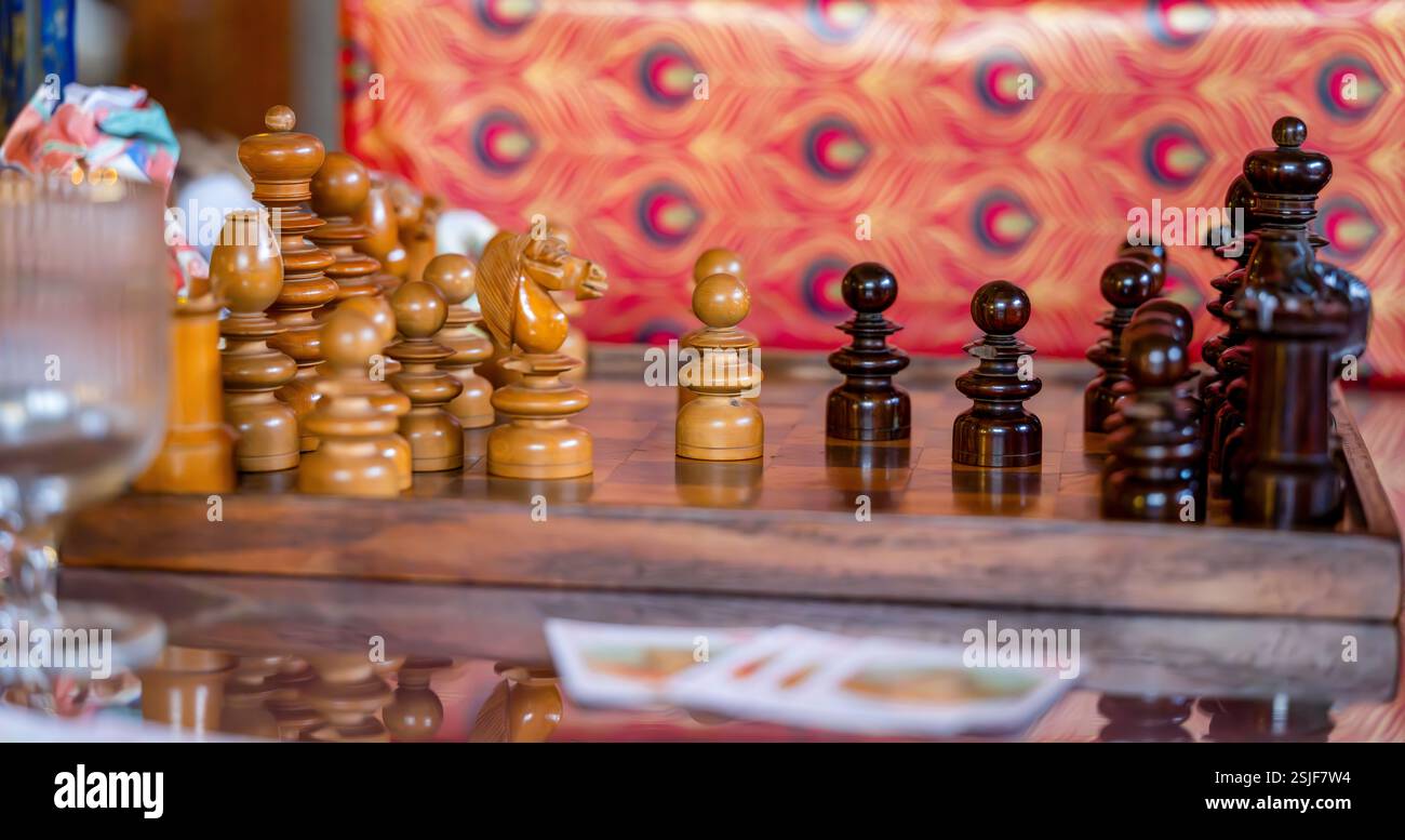 Handgefertigte hölzerne Schachstücke auf rustikalem Schachbrett mit festlichem, lebendigem Hintergrund Stockfoto