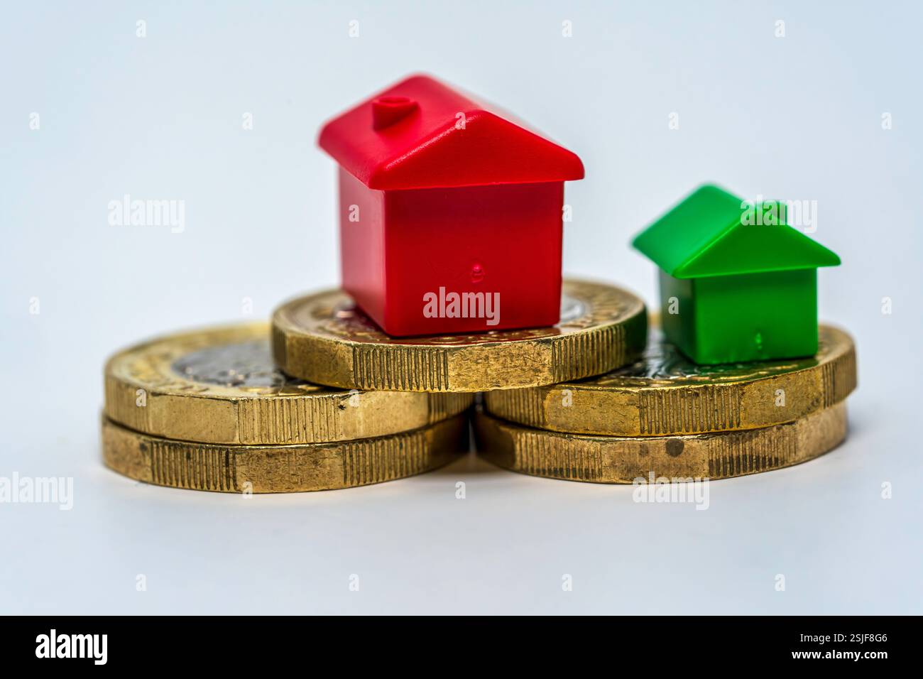 Symbolische Darstellung von Immobilieninvestitionen mit Kunststoffhäusern und gestapelten Münzen Stockfoto