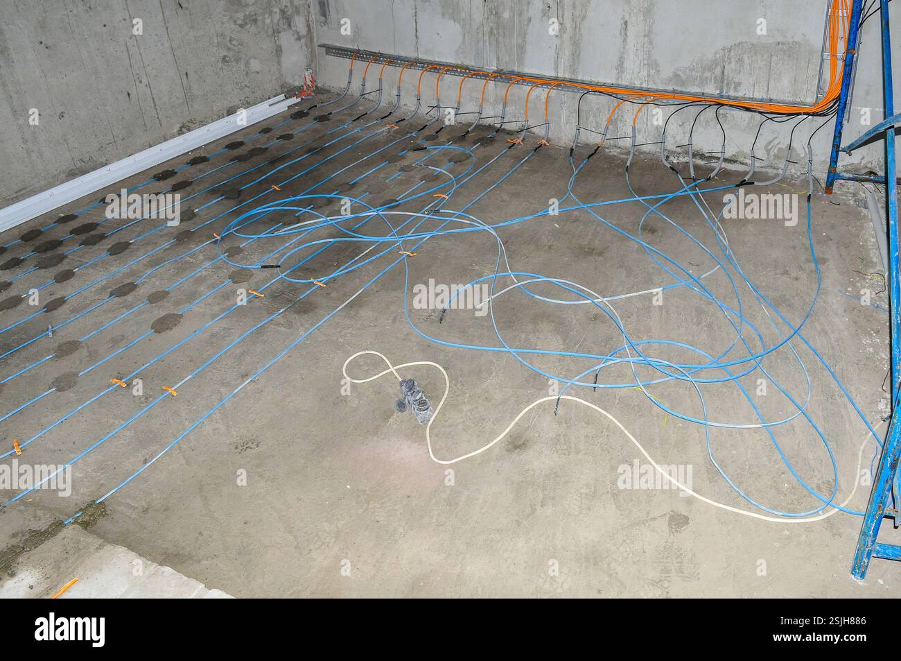 Installation einer Fußbodenheizung mit blauen Rohren, die mit orangefarbenen Befestigungselementen befestigt sind, in einem Betonraum, bereit für den Estrich. Stockfoto
