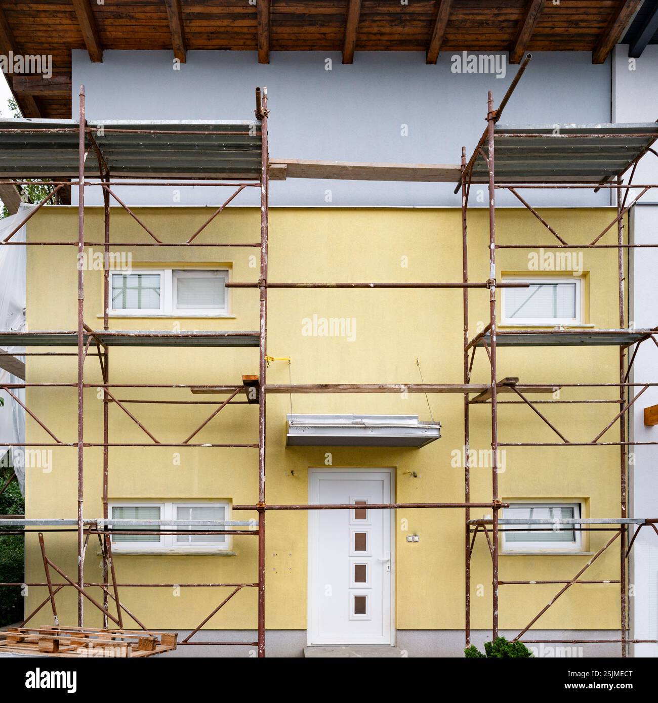 Ein Haus, das gerade renoviert wird, mit Metallgerüsten, die die Vorderfassade abdecken. Die untere Hälfte ist gelb, während der obere Teil neu hellblau lackiert ist. Stockfoto