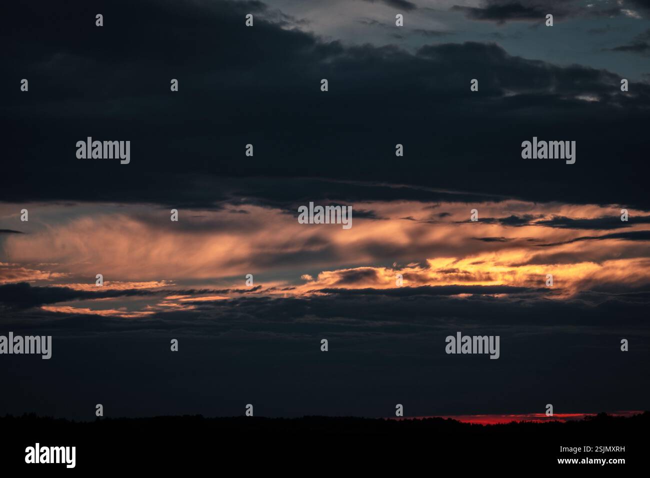 Ein stimmungsvoller Sonnenuntergangshimmel mit Schichten dunkler Wolken und einem goldenen Glühen, das durchbricht. Der Kontrast zwischen Schatten und Licht erzeugt einen filmischen Himmel Stockfoto