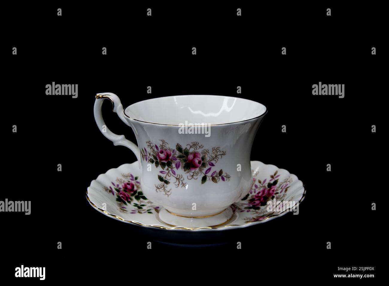 Elegante Vintage Porzellan Teetasse und Untertasse mit zarten Blumenmustern und goldenen Besätzen, isoliert auf schwarzem Hintergrund. Stockfoto