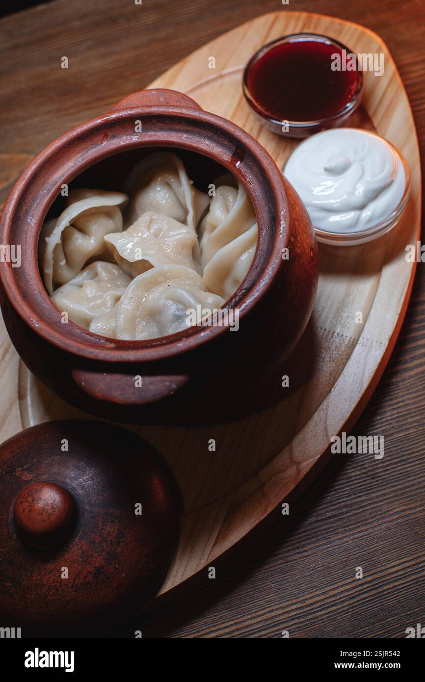 Heiße, saftige Teigtaschen in einen Topf gekuschelt. Daneben gibt es einen Löffel Sauerrahm, um dieses Gericht noch schmackhafter zu machen. Stockfoto