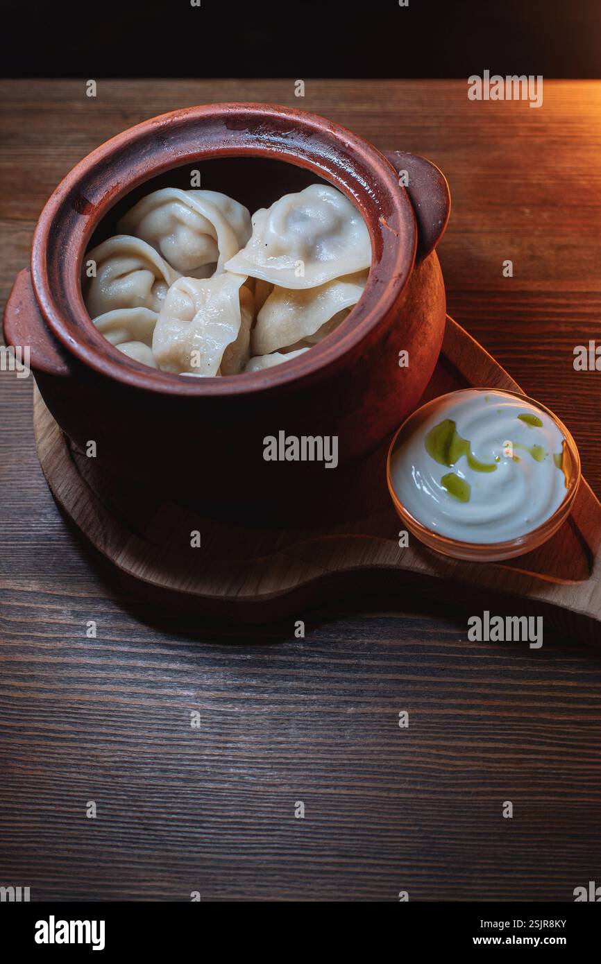 Heiße, saftige Teigtaschen in einen Topf gekuschelt. Daneben gibt es einen Löffel Sauerrahm, um dieses Gericht noch schmackhafter zu machen. Stockfoto