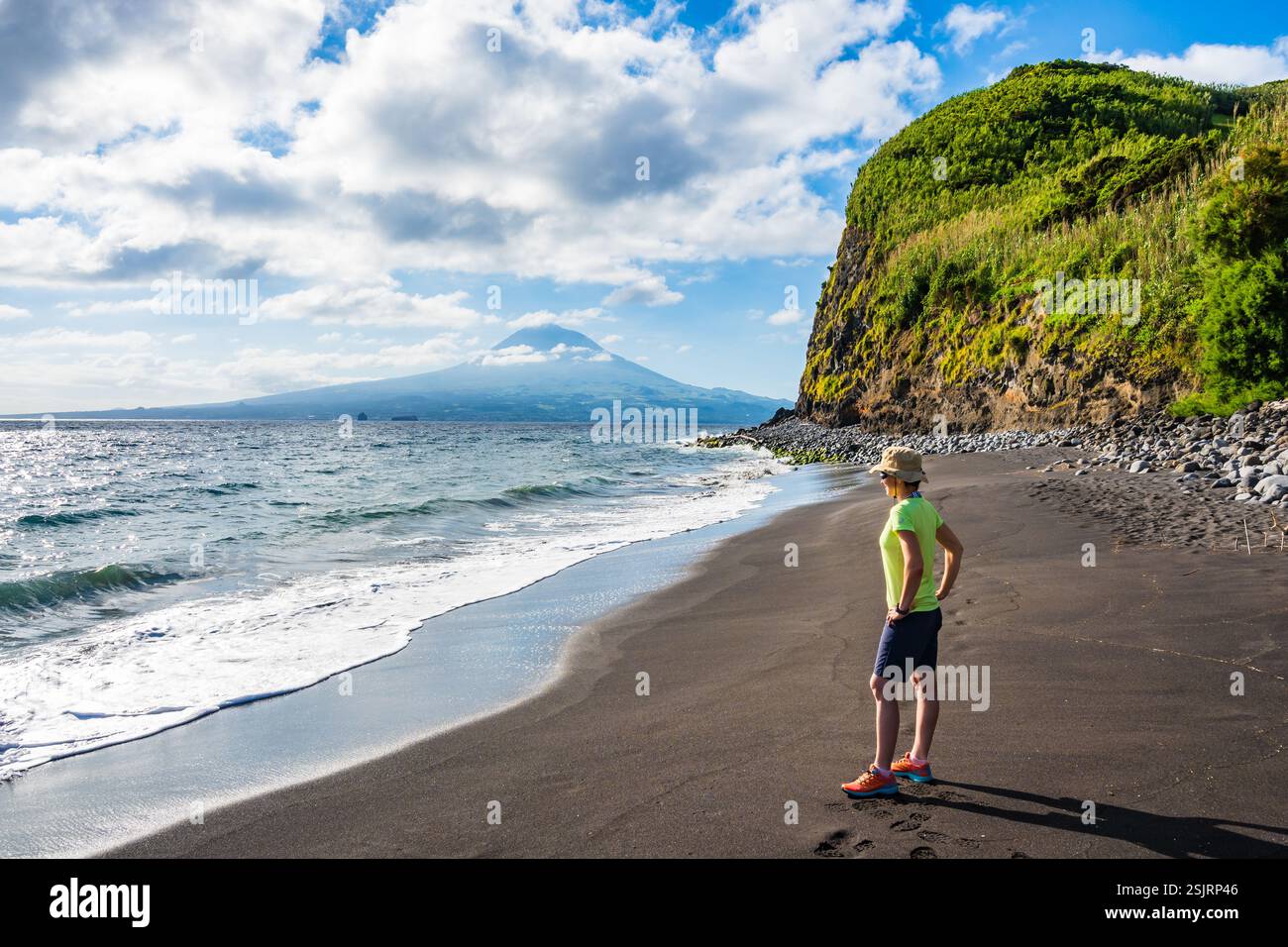 Junge Frau, die auf Sand am Strand von Almoxarife mit azurblauem Meereswasser an der Küste der Insel Faial, Azoren, Portugal steht Stockfoto