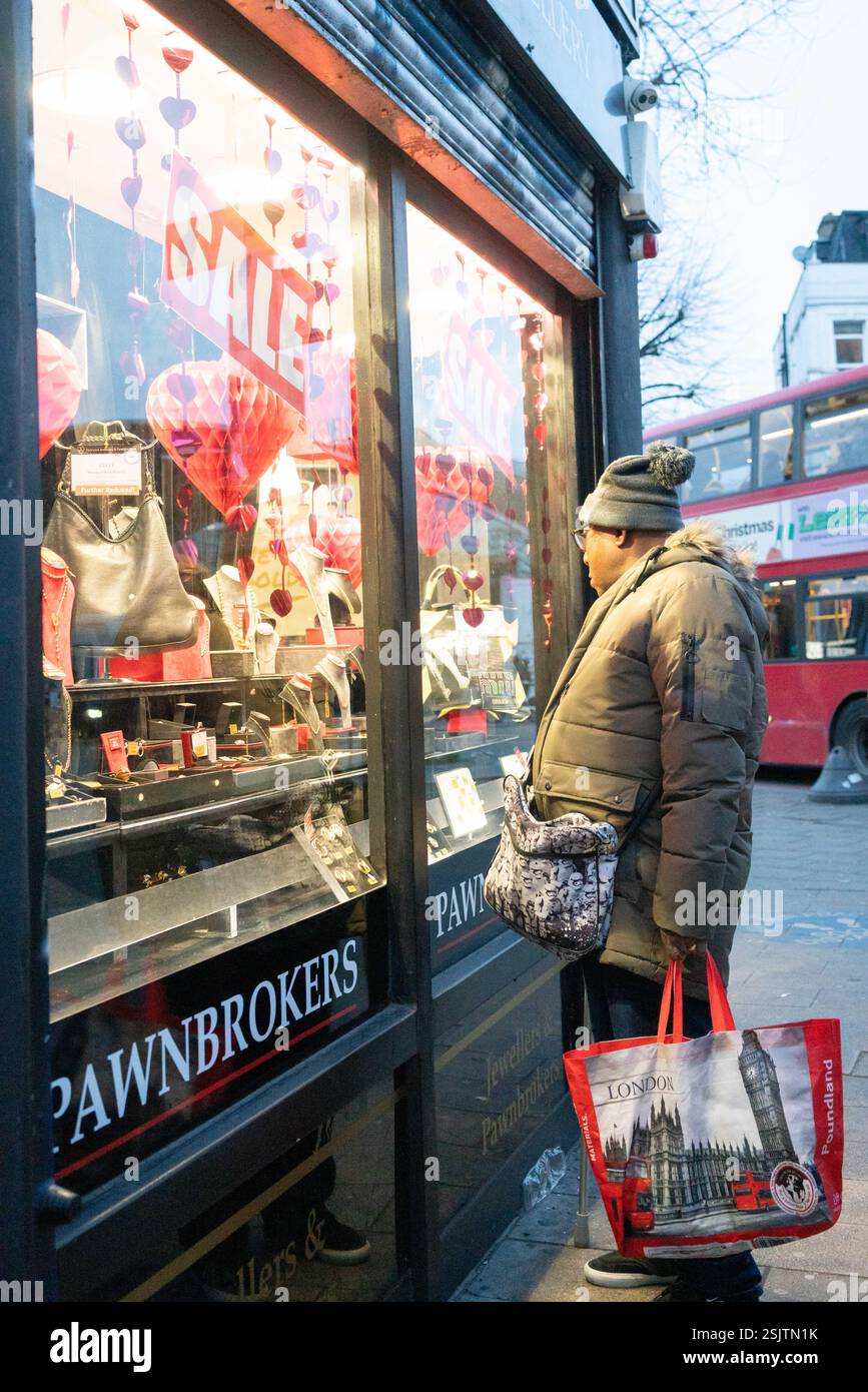 Ein afro-karibischer Mann mit einer Einkaufstasche schaut in das Fenster eines Pfandmaklers in Peckham Rye im Süden Londons. Stockfoto