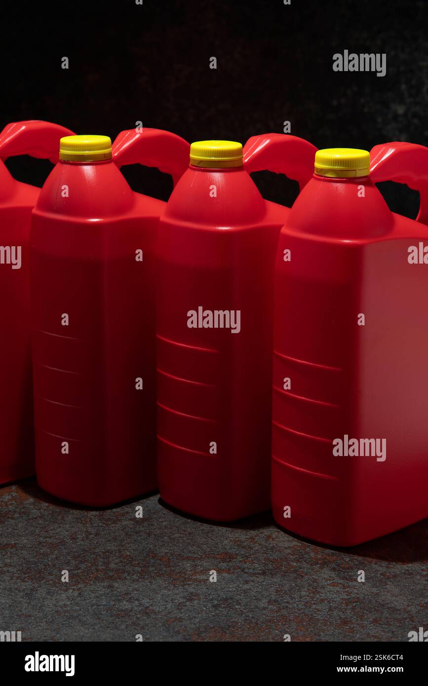 Dreiviertelansicht von 3 roten Motorölflaschen aus Kunststoff mit Griff und gelbem Schraubverschluss ohne Etikett auf dunkler Keramik vor schwarzem Hintergrund Stockfoto