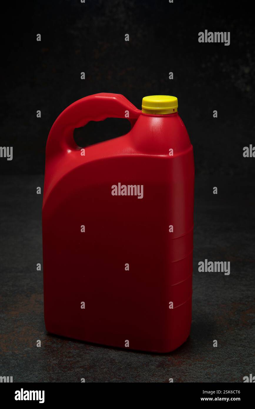 Dreiviertelansicht der roten Motorölflasche aus Kunststoff mit Griff und gelbem Schraubverschluss ohne Etikett auf dunkler Keramik vor schwarzem Hintergrund Stockfoto