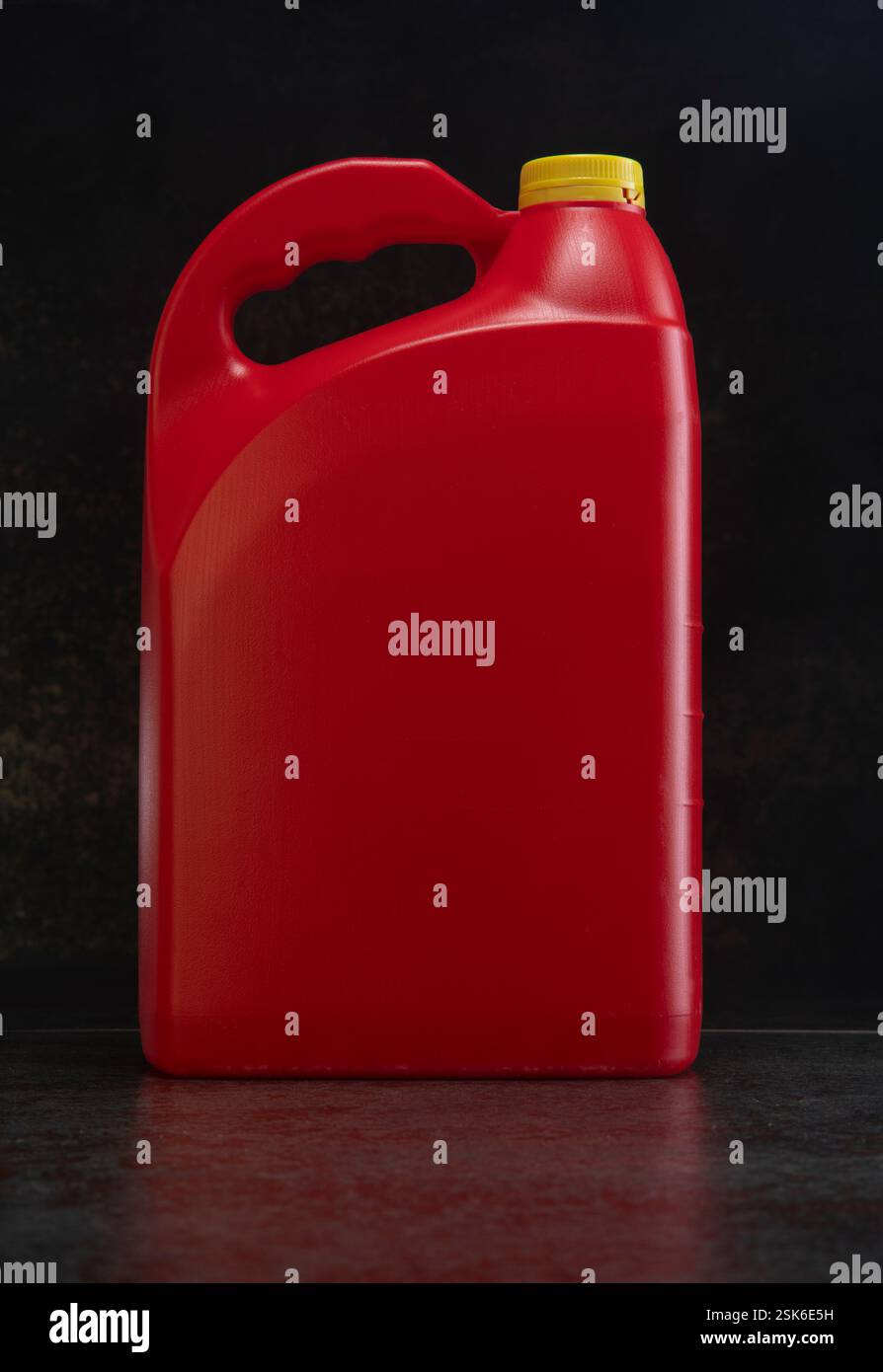 Vorderansicht der roten Motorölflasche aus Kunststoff, Behälter mit Griff und gelbem Schraubverschluss ohne Etikett auf dunkler Keramikoberfläche Stockfoto