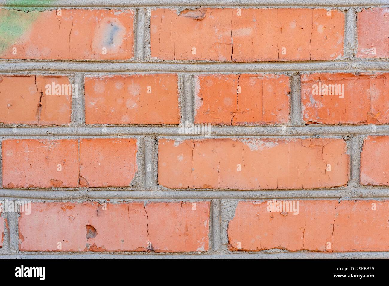 Eine Nahaufnahme einer verwitterten Ziegelwand zeigt die Textur und Details der Ziegelsteine. Risse und verschiedene Orangentöne heben die ag der Wand hervor Stockfoto