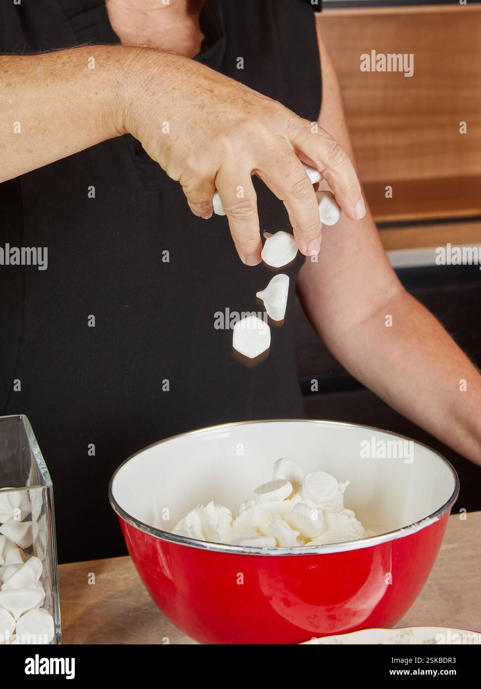 Marshmallows werden in eine Mischschüssel geworfen, was die lustige Dessertzubereitung in einer hellen und fröhlichen Küche veranschaulicht. Stockfoto Marshmallows werden in eine Mischschüssel geworfen, was die lustige Dessertzubereitung in einer hellen und fröhlichen Küche veranschaulicht. Stockfoto