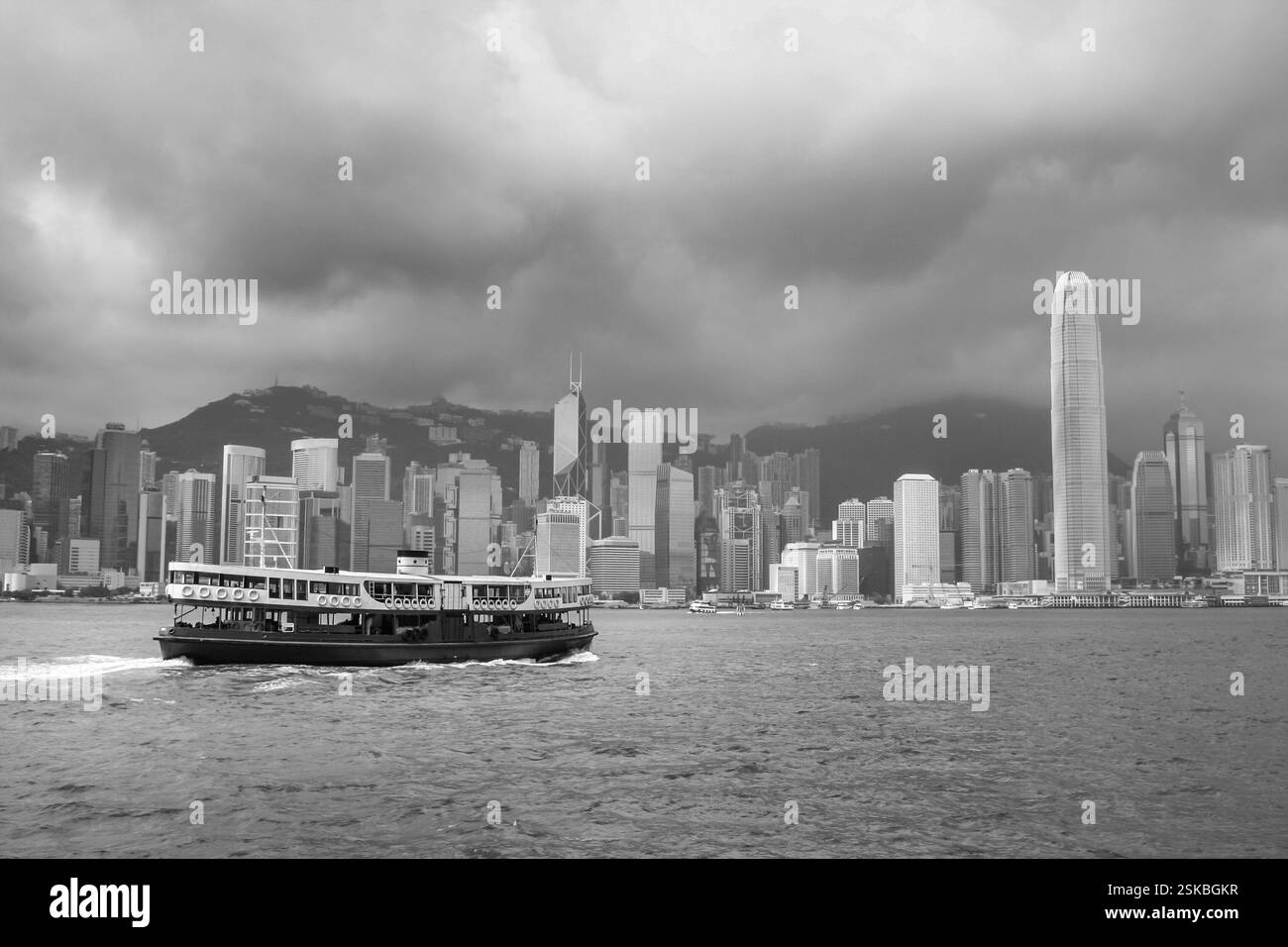 Skyline von Hong Kong Island und berühmte Fähre auf Victoria Harbour in Schwarz-weiß Stockfoto
