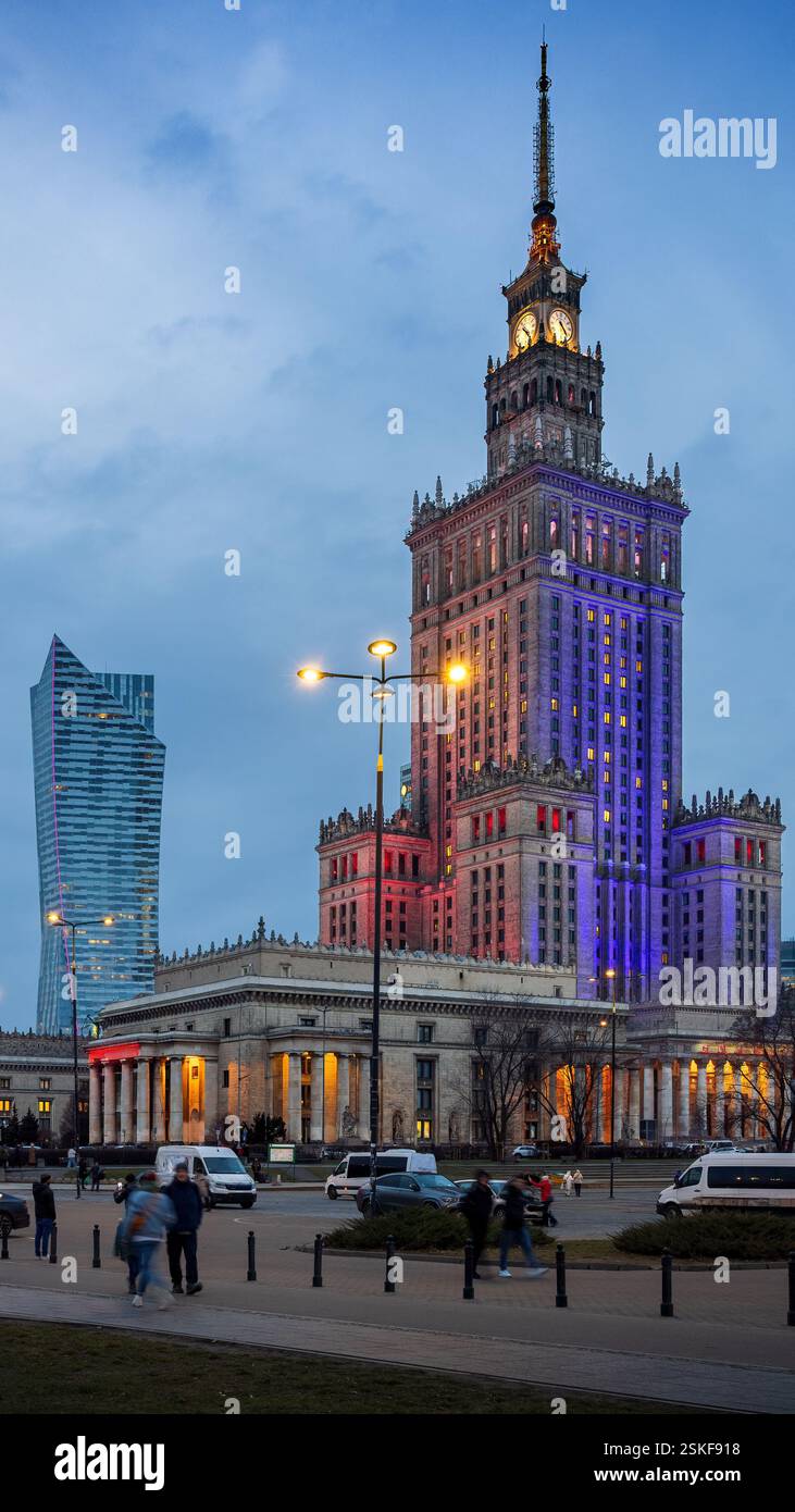 Nacht in Warschau, Polen. Der Palast der Kultur und Wissenschaft ist in leuchtenden roten, blauen und violetten Lichtern beleuchtet, die sich vom dunklen Himmel abheben. Stockfoto