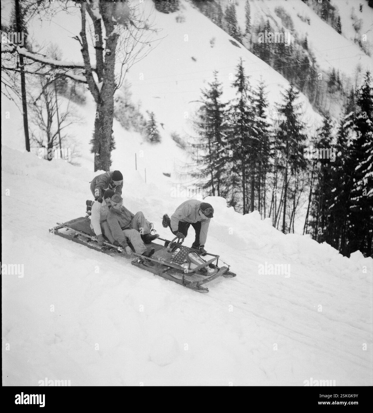 Kurz nach dem Start; da die Bahn stark verschneit war, müssen die Konkurrenten auf der offenen Strecke durch stossen den Bob wieder in Fahrt bringen#kurz nach dem Start; da die Bahn stark verschneit war, mussten die Teilnehmer während des Rennens den Bob schieben----- Schweizer Bob-Meisterschaft, Les Avants 1951: Haari und Team#Swiss Bobsleigh Championship, Les Avants 1951: Haari und Tream-RDB VON DUKAS Stockfoto
