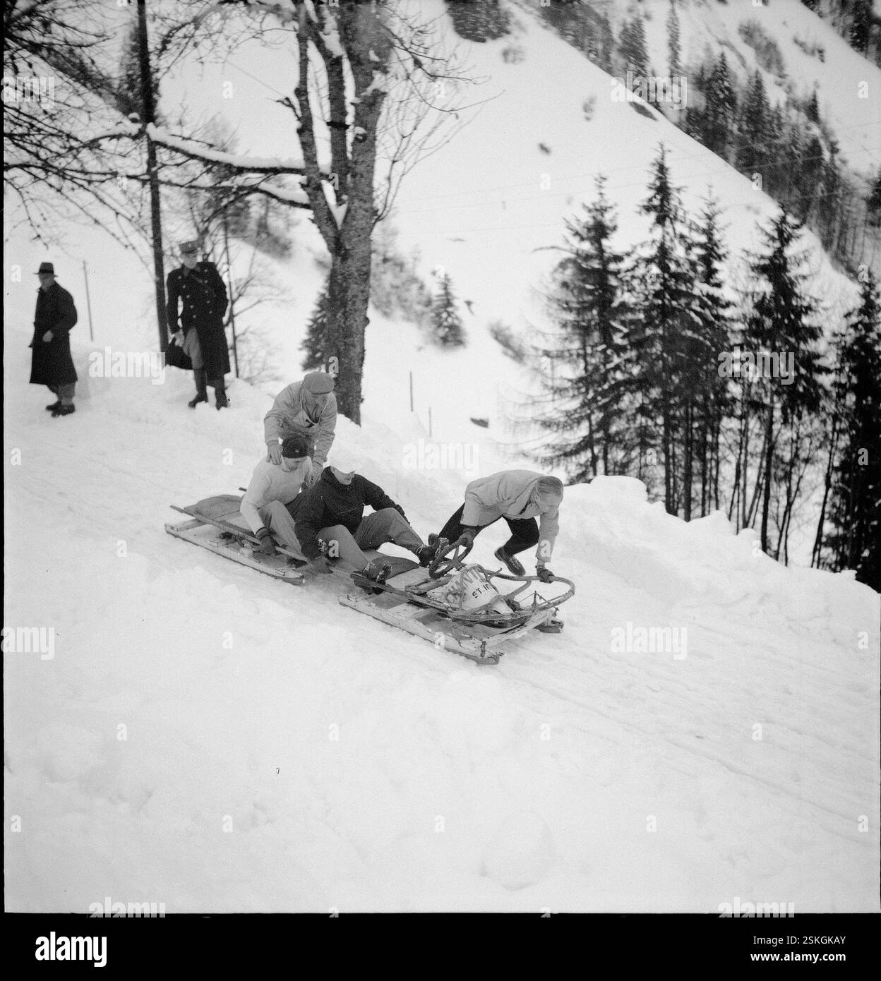 Kurz nach dem Start; da die Bahn stark verschneit war, müssen die Konkurrenten auf der offenen Strecke durch stossen den Bob wieder in Fahrt bringen#kurz nach dem Start; da die Bahn stark verschneit war, mussten die Teilnehmer während des Rennens den Bob schieben----- Schweizer Bob-Meisterschaft, Les Avants 1951: Canton (St. Imier)#Swiss Bobsleigh Championship, Les Avants 1951: Canton (St. Imier)- RDB BY DUKAS Stockfoto