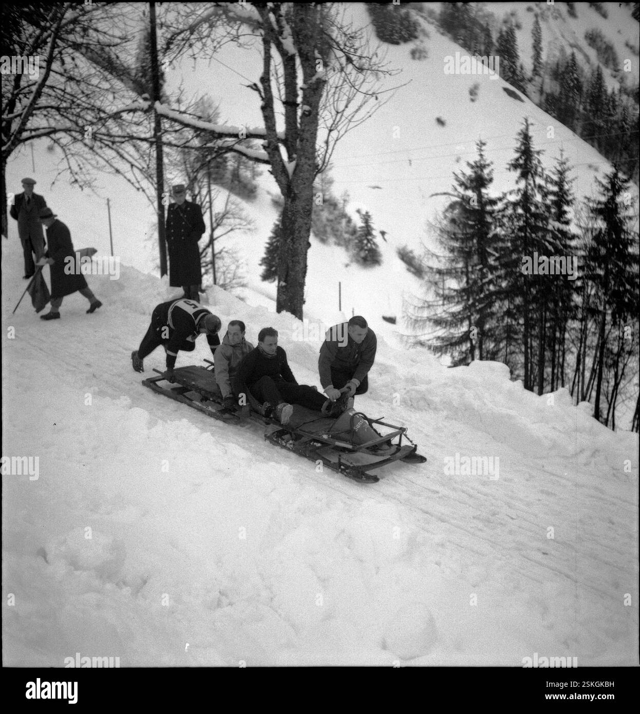 Kurz nach dem Start; da die Bahn stark verschneit war, müssen die Konkurrenten auf der offenen Strecke durch stossen den Bob wieder in Fahrt bringen#kurz nach dem Start; da die Bahn stark verschneit war, mussten die Teilnehmer während des Rennens den Bob schieben--- Schweizer Bob-Meisterschaft, Les Avants 1951: Huber#Swiss Bobsleigh Championship, Les Avants 1951: Huber- RDB VON DUKAS Stockfoto