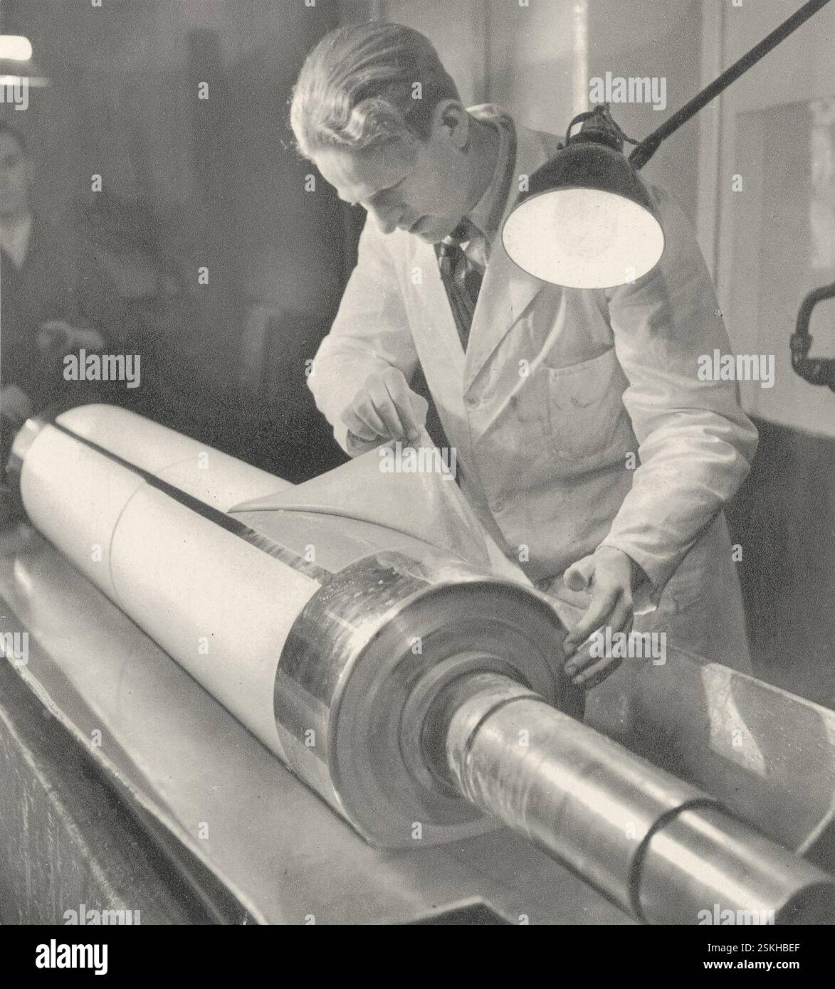 Damit das kopierte Pigmentpapier von Hand oder auch maschinell unter Anwendung von Wasser auf die Kupferzylinder gebracht werden kann, müssen diese zuerst gründlich entfettet werden. Ist das Pigmentpapier auf den Zylinder übertragen, dann wird es in warmem Wasser lange gebadet, bis sich die Papierunterlage loslösen lässt und nur die Pigmentschicht auf dem Kupfer haften bleibt--- 'Entwicklung': Pigmentpapier wird vom Zylinder gelöst, um 1936#'Entwicklung': Pigmentpapier wird vom Zylinder gelöst, um 1936- RDB VON DUKAS Stockfoto
