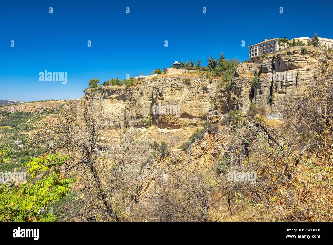 Ronda Stadt in Spanien. Ein malerischer Blick auf eine Landschaft an den Klippen unter einem klaren blauen Himmel. Gebäude thronen auf den hohen, zerklüfteten Klippen. Stockfoto