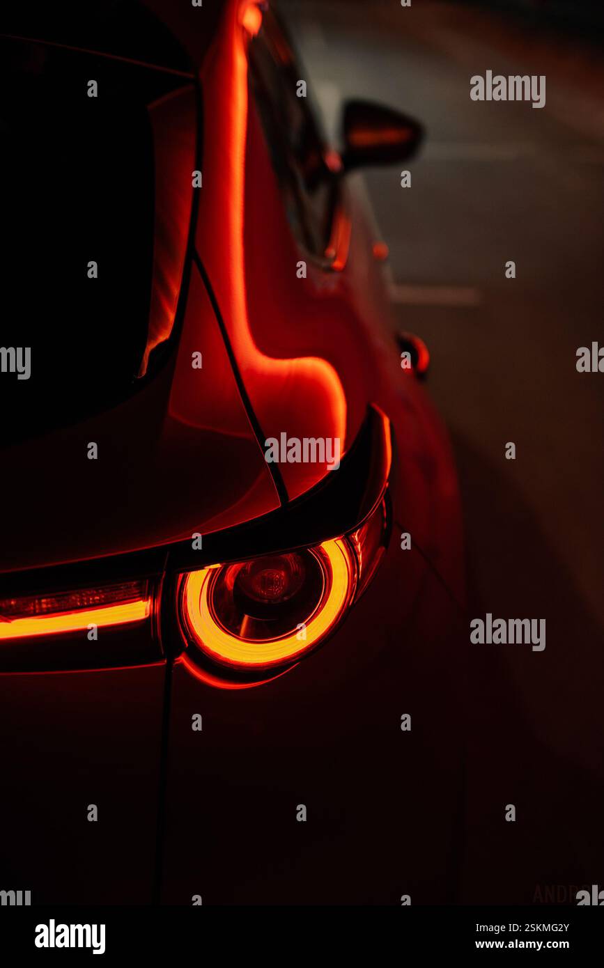Rücklicht eines modernen roten Autos bei Nacht. Vertikale Nahaufnahme leuchtender LED-Rückleuchten in warmorangenem Licht – Reflexion von Stadtlichtern. Stockfoto