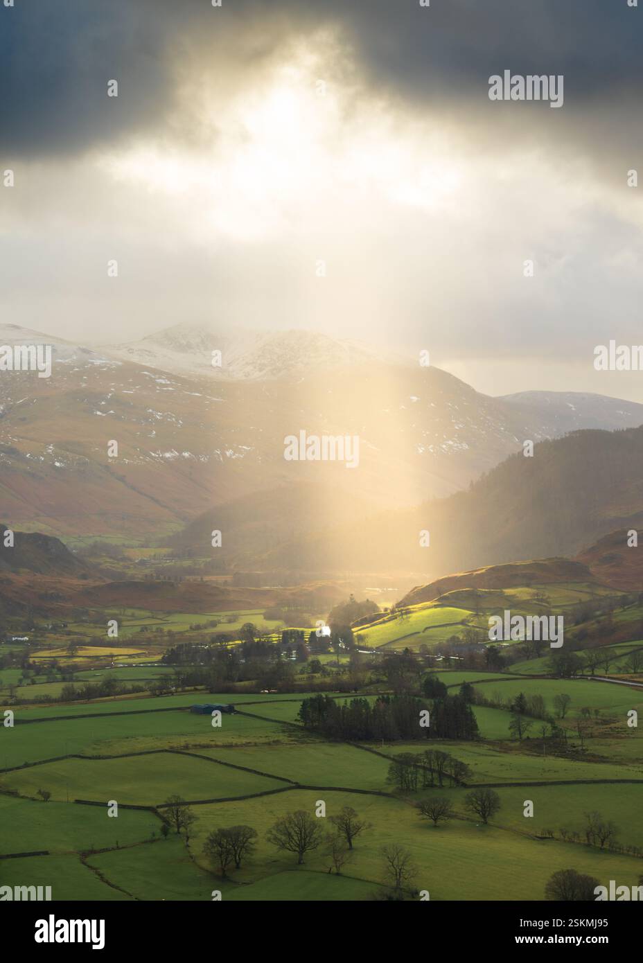 Helle Sonnenstrahlen, die durch dramatische Wolken auf grüne Felder in der britischen Landschaft brechen. Lake District, Großbritannien. Stockfoto