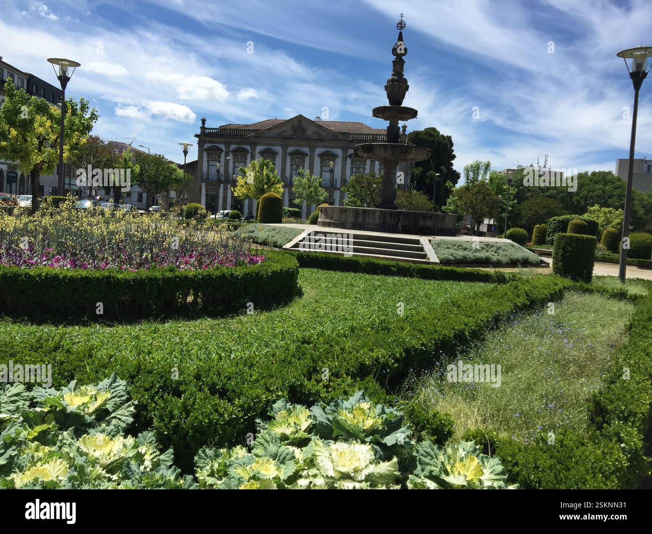 Park mit Brunnen und Gebäude, Braga, Portugal. Üppiges Grün und farbenfrohe Blumen schaffen eine ruhige urbane Oase. Die Natur blüht inmitten der Stadt. Stockfoto