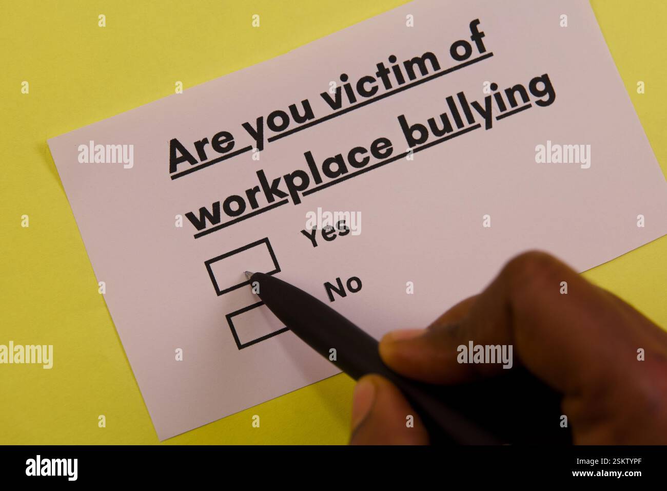 Eine Person, die eine Antwort auf einer Umfrage zum Mobbing am Arbeitsplatz auf einem hellgelben Hintergrund markiert. Stockfoto