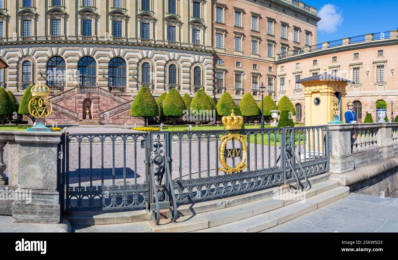 Eingang des Logården-Gartens des Königlichen Palastes in Stockholm, Schweden, mit einer vergoldeten Krone auf dem Zaun im Vordergrund, flankiert von einer königlichen Garde. Stockfoto