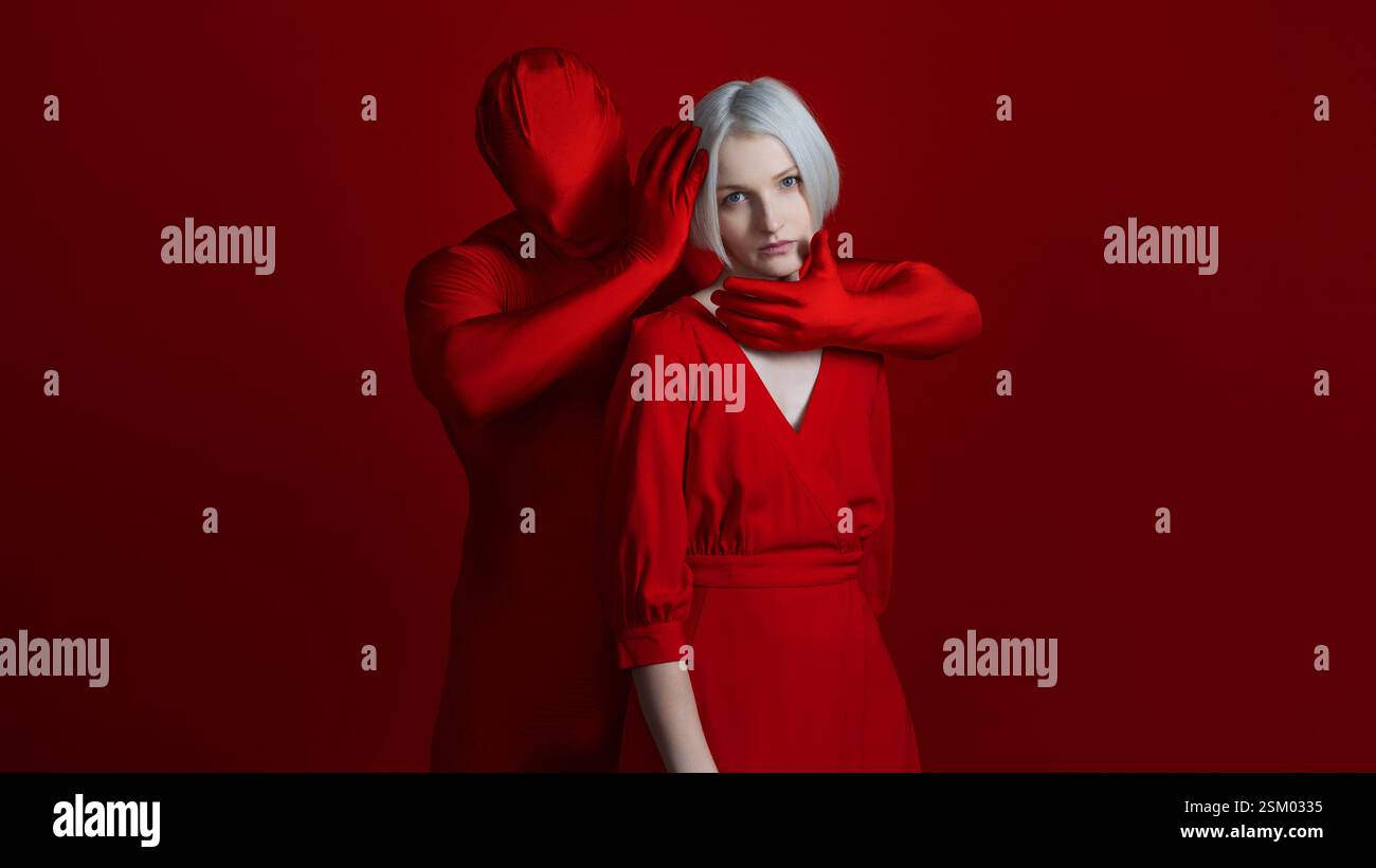 Ein Teil von mir, individuell oder von außen auferlegt. Etwas von innen und etwas von außen als Teil einer einzigen Persönlichkeit, eines Konzepts. Eine Frau in einem roten Kleid und eine gesichtslose Figur in Rot berührt sie mit seinen Händen, Foto auf Rot Stockfoto