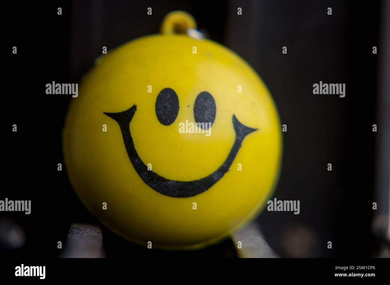Gelber Smiley-Gesicht-Ball-Schlüsselanhänger im Nahaufnahme mit selektiver Schärfentiefe vor dunklem Hintergrund. Stockfoto