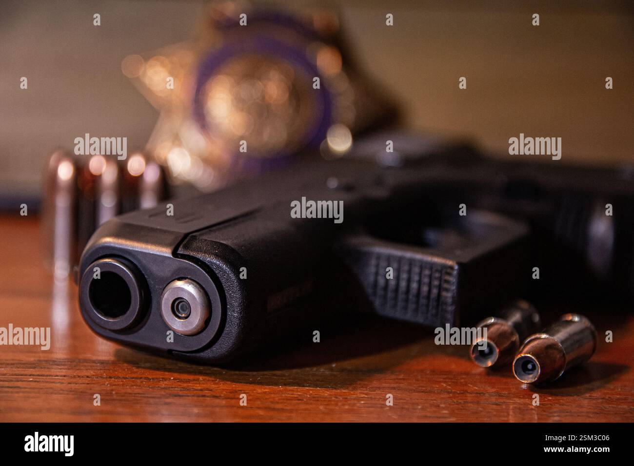 Eine schwarze halbautomatische Pistole liegt auf einem Tisch mit Hohlpunktmunition. Ein Strafverfolgungsausweis und weitere Kugeln sind im Hintergrund zu sehen. Stockfoto
