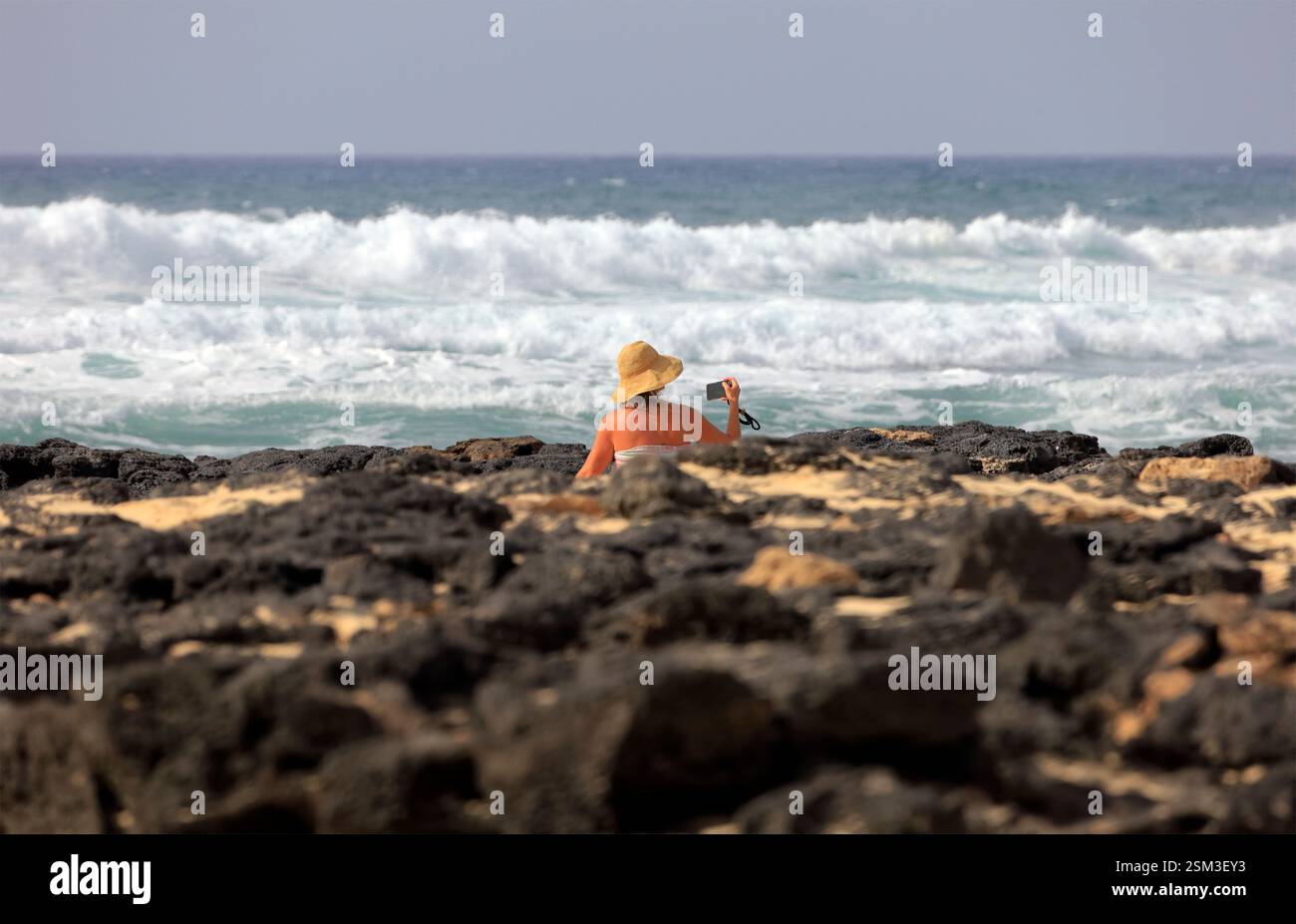 Einsame reife Frau, die sich zwischen vulkanischen Felsen am Ufer von El Cotillo, Oliva, Fuerteventura, den Kanarischen Inseln, Spanien sonnt. Stockfoto