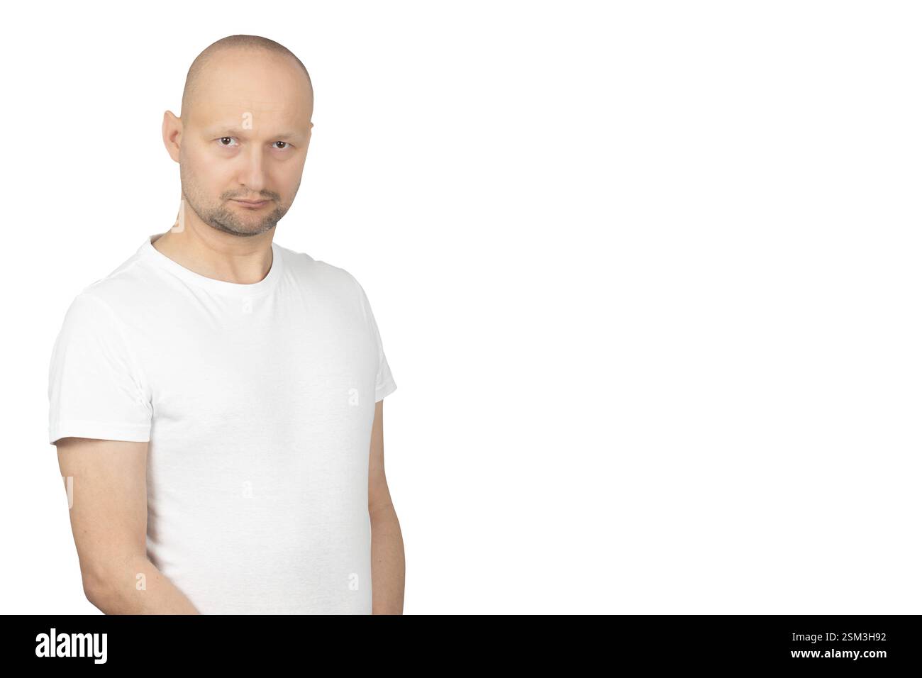 Ein kahlköpfiger Weißer mit kurzem Bart trägt ein weißes T-Shirt und blickt mit ernstem Ausdruck direkt in die Kamera. Stockfoto