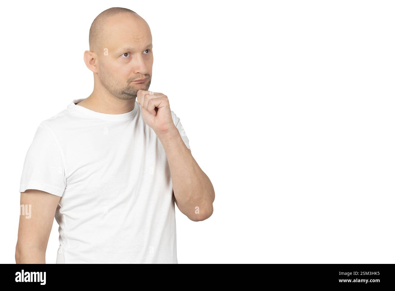 Ein kahler Weißer in einem weißen T-Shirt steht vor einem weißen Hintergrund, berührt sein Kinn und blickt tief nachdenklich nach oben. Stockfoto