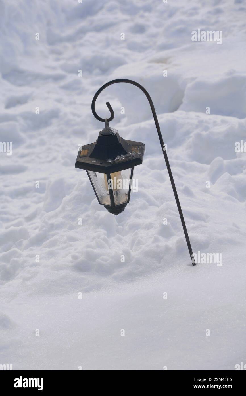Eine schwarze solarbetriebene Gartenleuchte ist alles, was sichtbar ist, nachdem ein Wintersturm den Garten mit Schnee bedeckt hat. Stockfoto