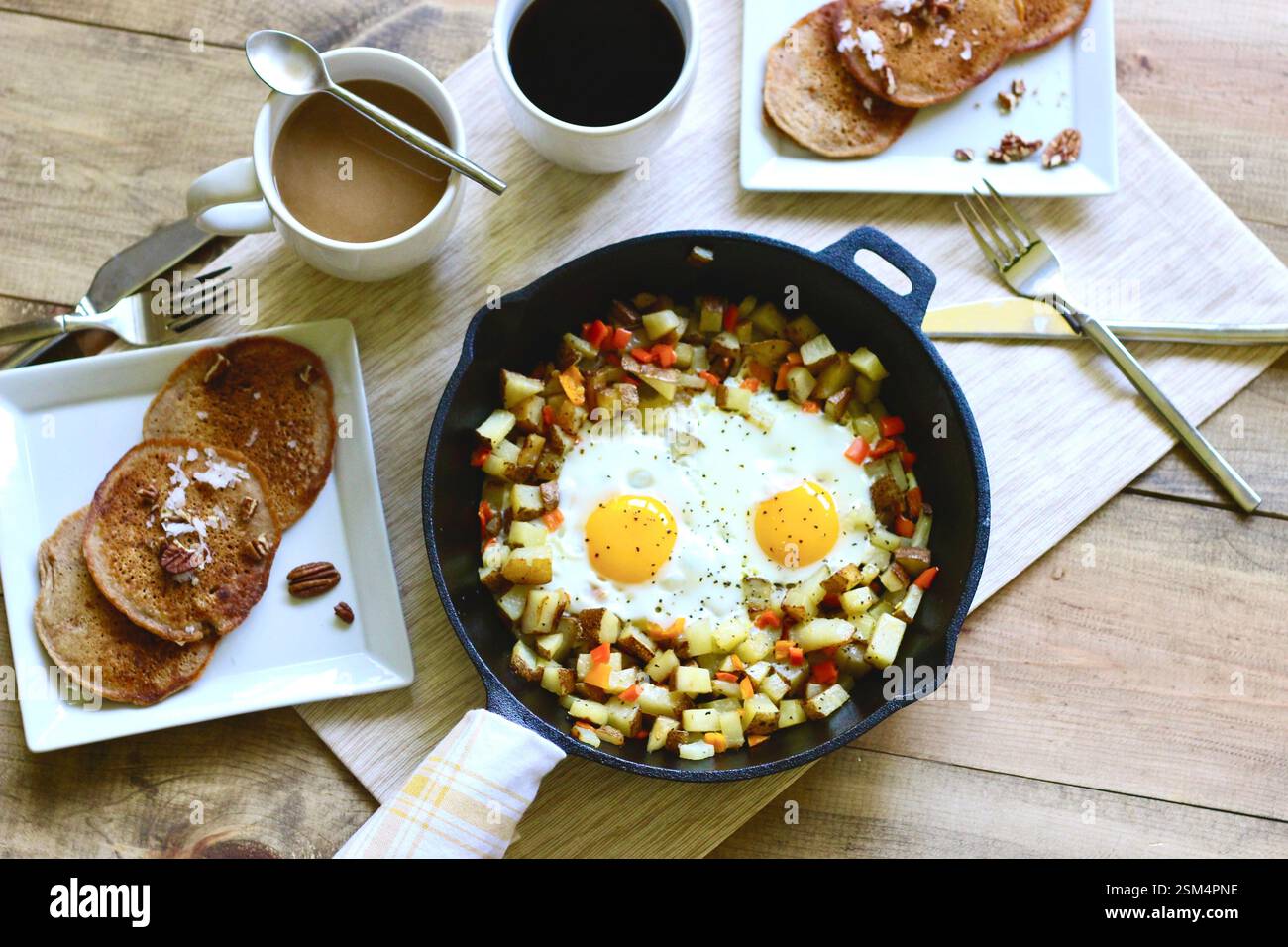 Rustikales Skillet-Frühstück mit gebratenen Eiern, Kartoffeln, Pfannkuchen und Kaffee – Brunch-Szene über Kopf Stockfoto