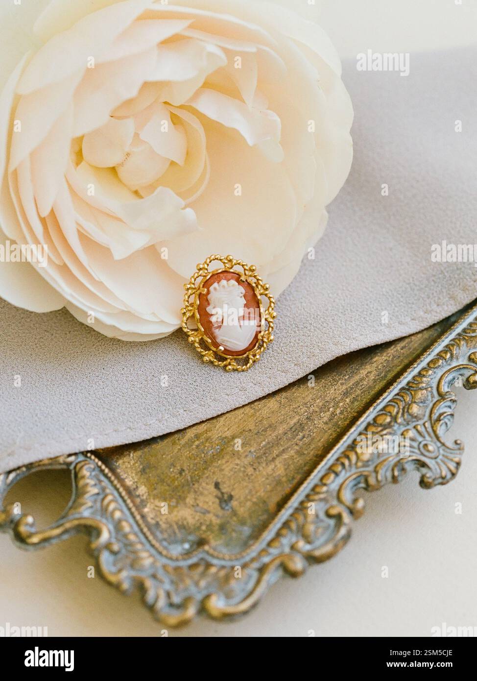 Eine Vintage-Cameo-Brosche liegt anmutig auf weichem Stoff mit Blume und verziertem Tablett und strahlt klassische Schönheit aus. Stockfoto