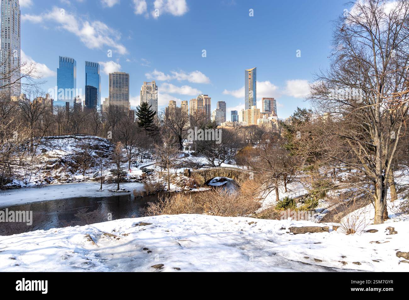 Die winterliche Schönheit des Central Park an einem sonnigen Tag im Februar 2025, mit dem Teich und der Gapstow Bridge inmitten von Wolkenkratzern und schneebedeckten Pfaden. Stockfoto
