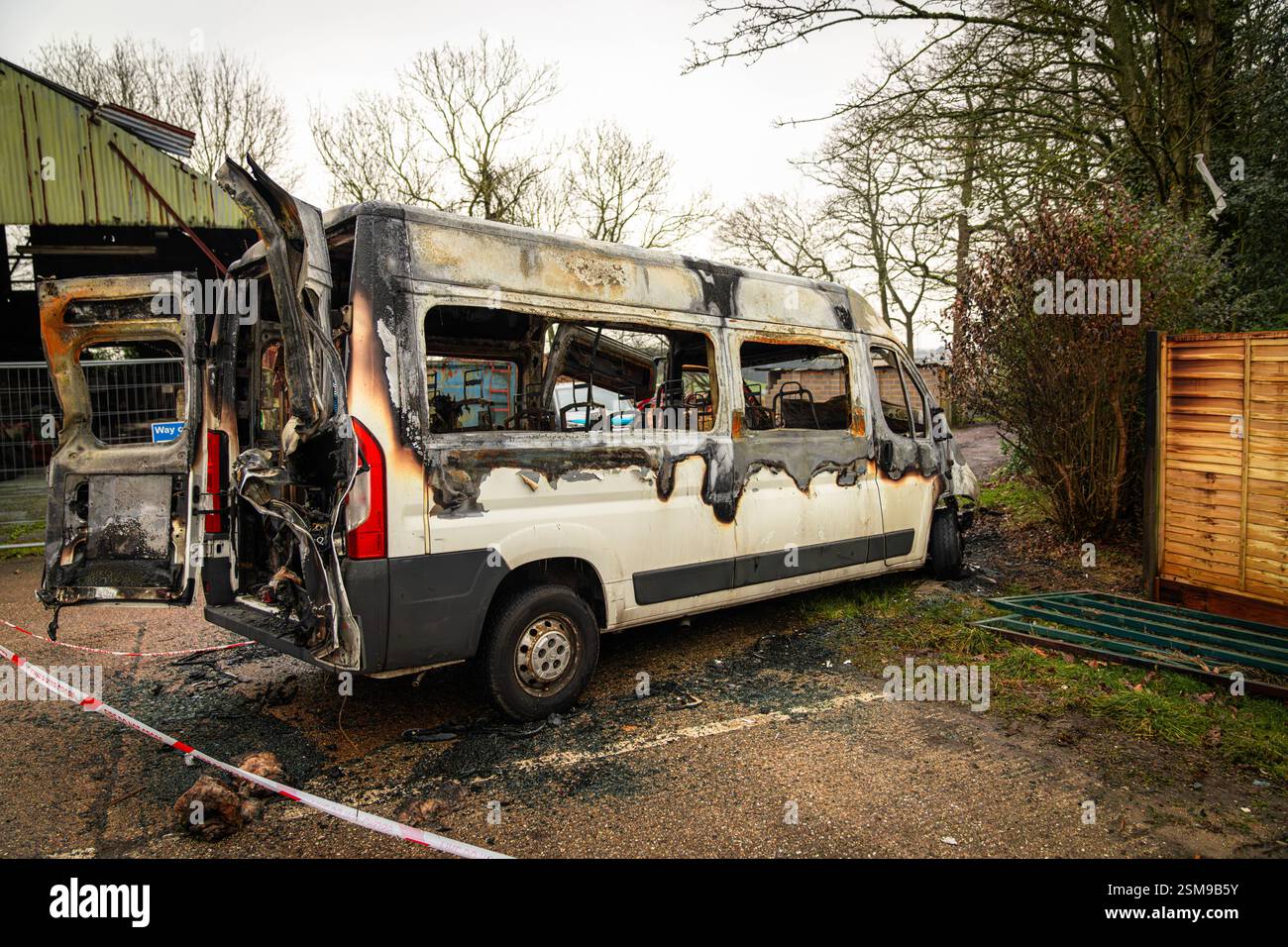 Weißer Van brannte völlig aus, parkte in der Nähe eines Holzzauns und eines Metalltors, mit einem rot-weißen Warnband auf dem Boden Stockfoto