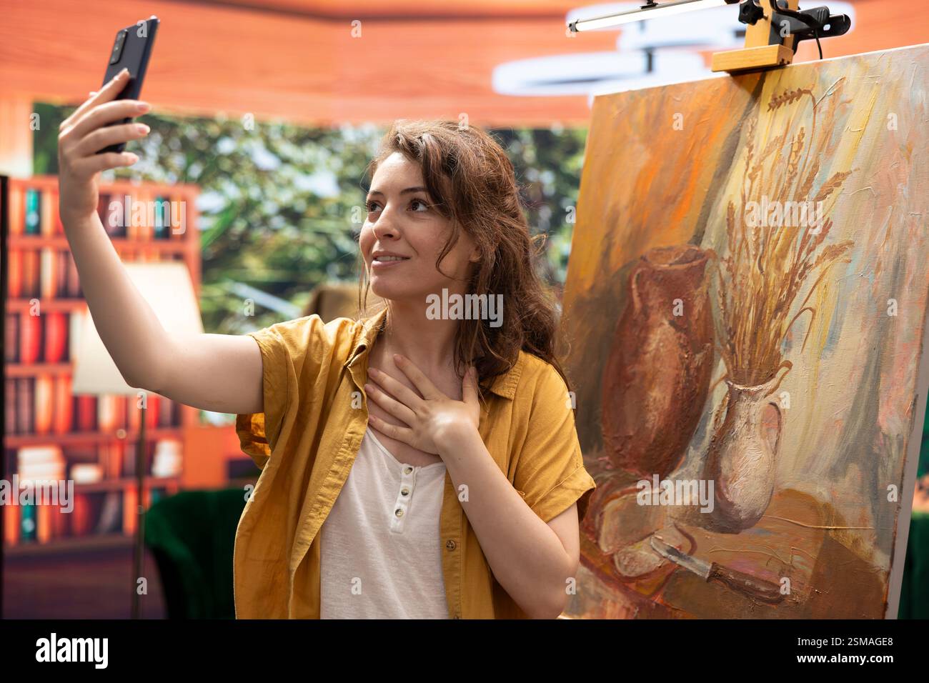 Influencer-Künstlerin filmt ihr fertiges rustikales Kunstwerk für ein Online-Branding und Selbstwerbung und erklärt die Maltechnik im Kunststudio. Malerin, die ihren künstlerischen Fortschritt anpreist. Stockfoto