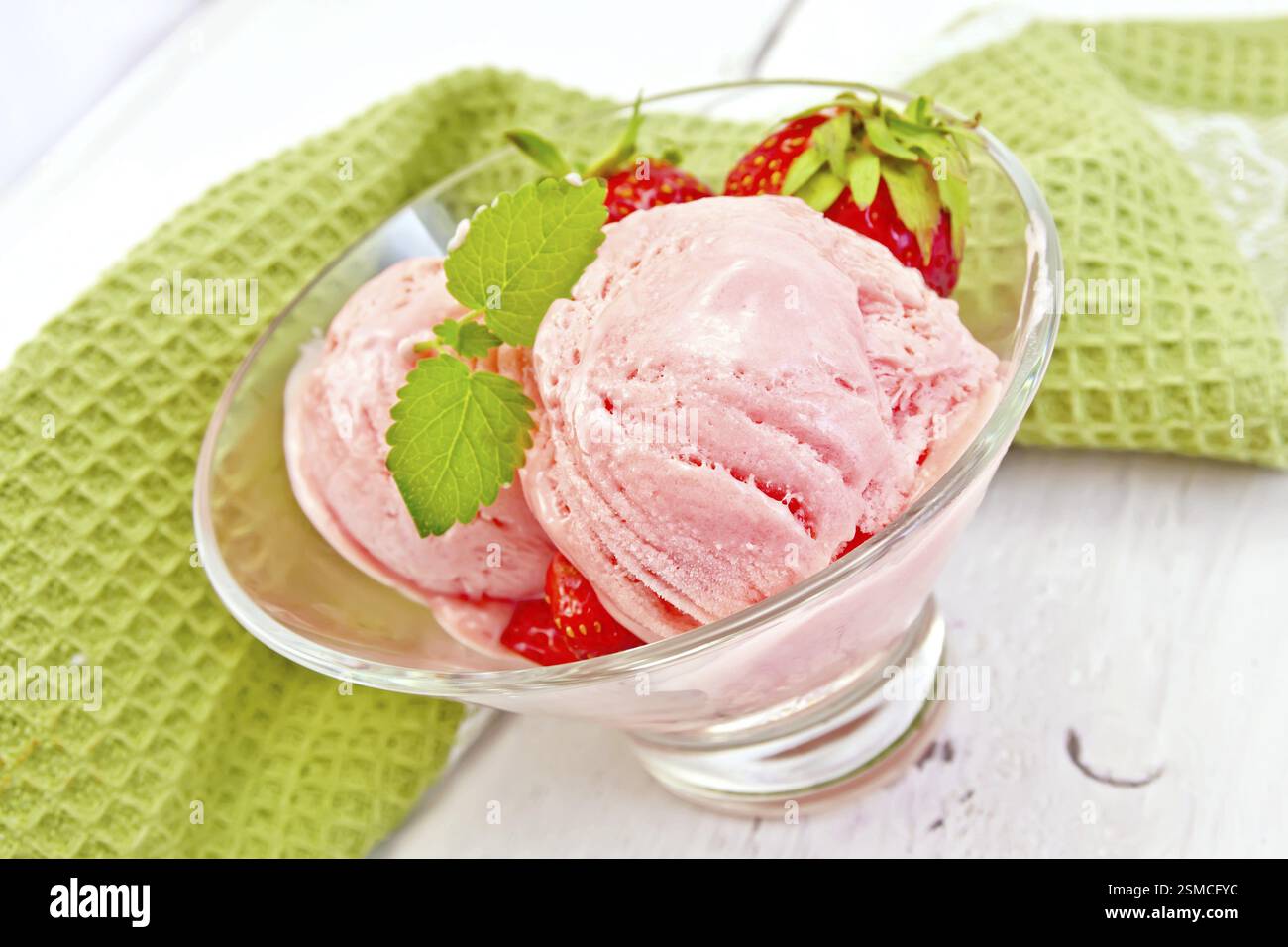 Erdbeereis in einem Glas mit Erdbeeren und Minze, Serviette auf dem Hintergrund helle Holzbretter Stockfoto