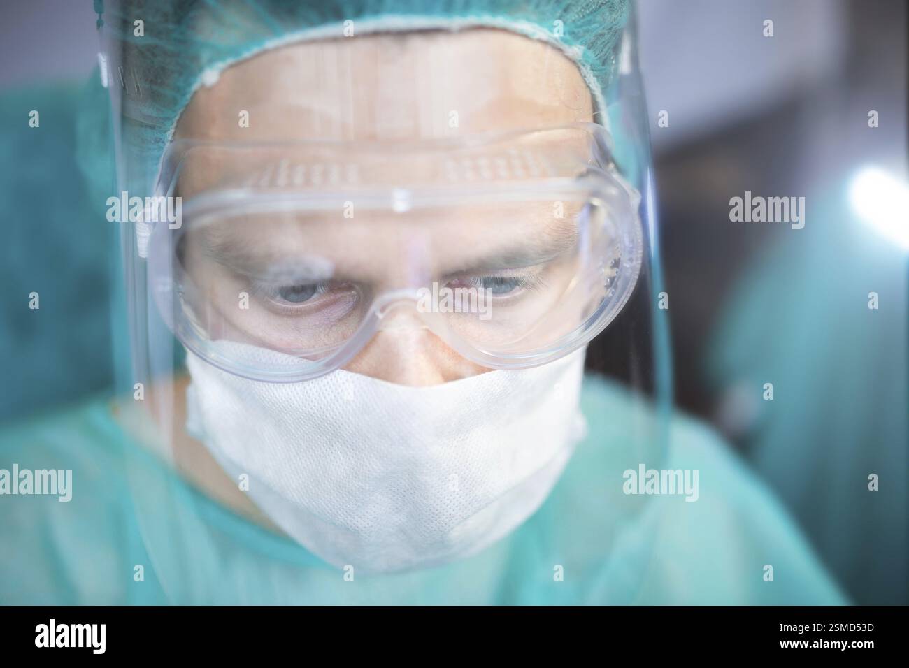 Medizinischer Mitarbeiter mit Schutzbrille und Maske, in einem nachdenklichen Moment mit blauer Kleidung festgehalten Stockfoto