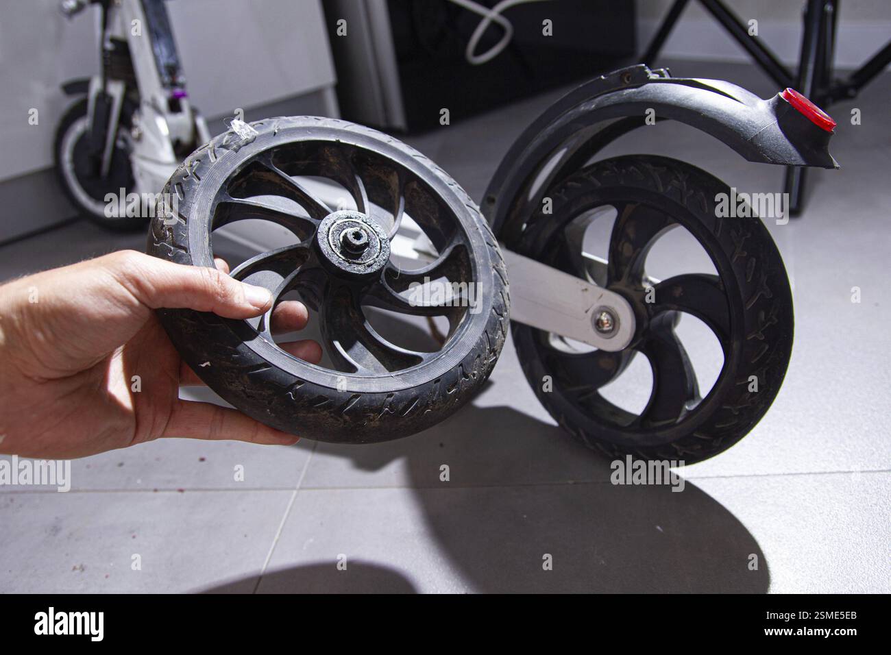 Das abgenommene Rollerrad in der Nähe des Hinterrads auf einem gefliesten Boden mit Schatten halten Stockfoto
