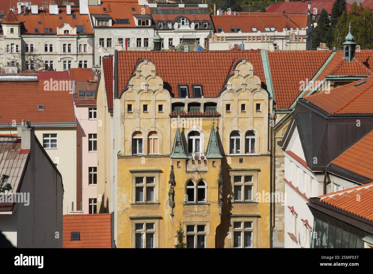 Blick aus der Vogelperspektive auf die Prager Dächer. Rot gekachelte Dächer prägen die Szene mit einigen grünen Akzenten. Ein herausragendes Gebäude mit kunstvoller gelber Fassade und Stockfoto