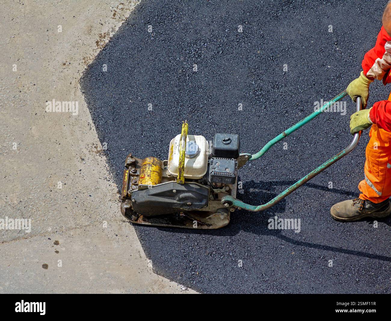 Industriearbeiter mit Plattenverdichter draußen auf Straßenasphalt Stockfoto