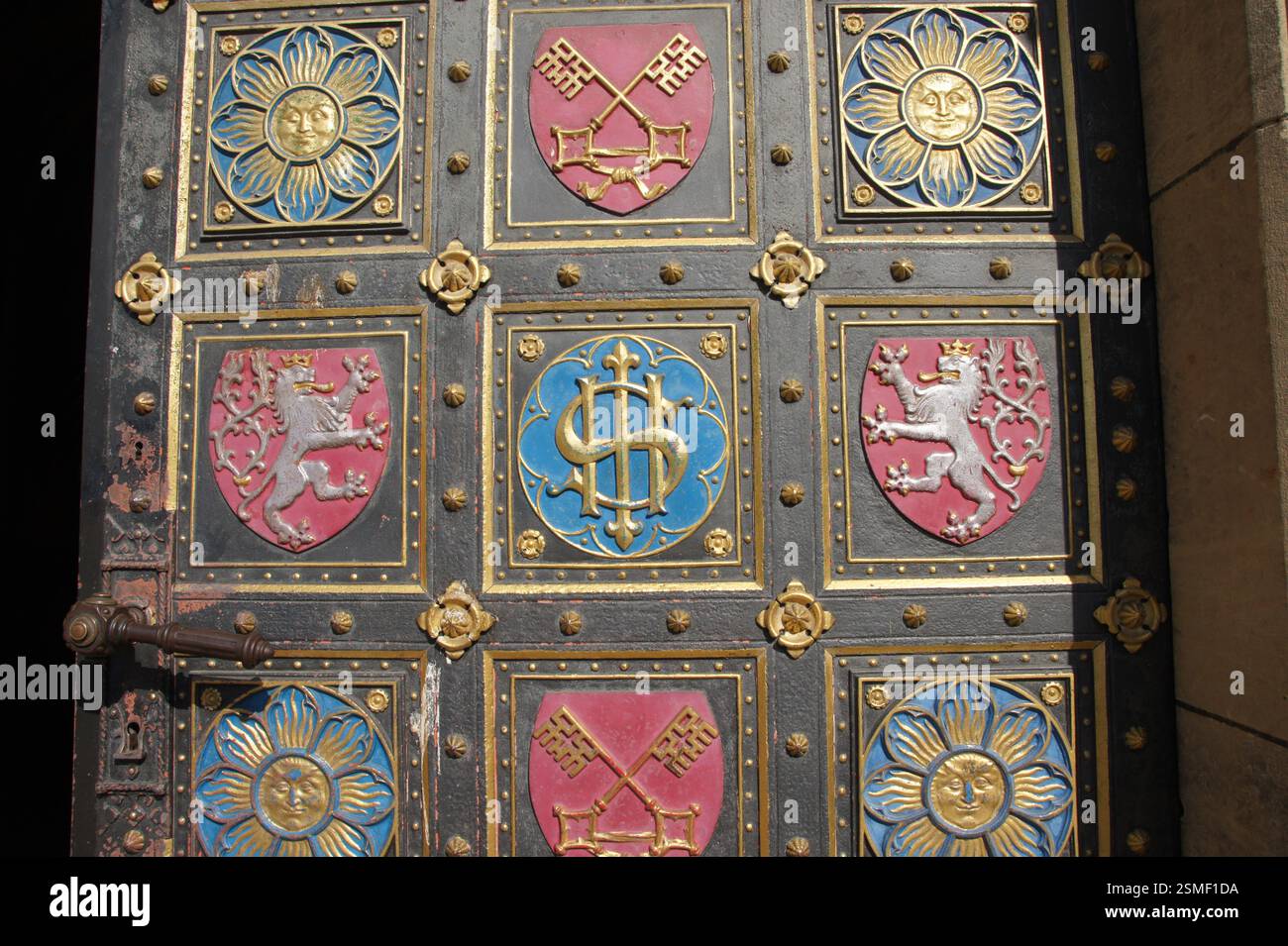 Schmiedeeiserne Tür mit kunstvollen Gold- und Silberdetails. Geometrische und florale Muster umgeben heraldische Symbole. Mögliche Verbindung zu religiös oder Ro Stockfoto