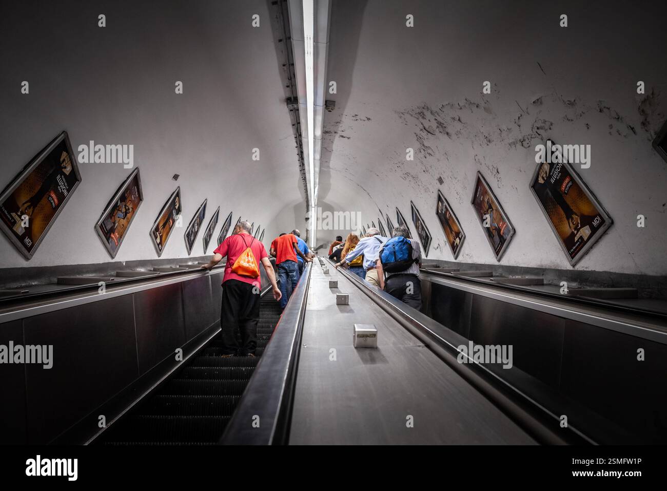 ROM, ITALIEN - 15. JUNI 2024: Pendler fahren auf den tiefen Rolltreppen der Metro Rom, umgeben von Werbetafeln an einer geschwungenen Tunnelwand. Rom U-Bahn, Stockfoto