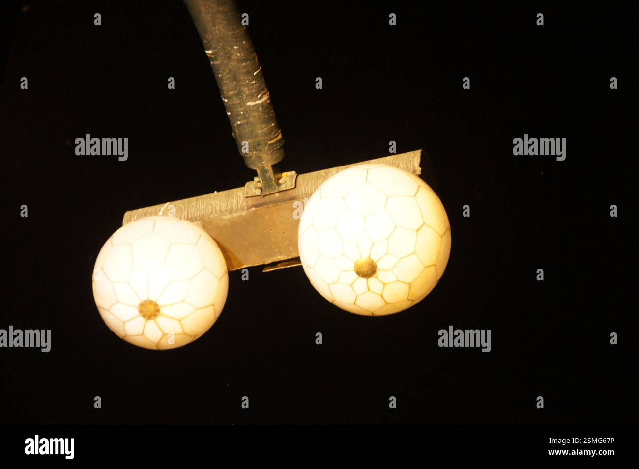 Vintage Pendelleuchte. Zwei weiße Milchglaskugeln mit komplizierten Mustern. Hängt an einem verwitterten Metallstab. Erinnert an Saibling aus der alten Welt Stockfoto