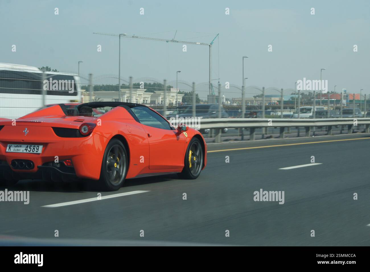 Ein roter Ferrari 458 Spider reißt einen Dubai Highway herunter. Der schlanke Sportwagen verkörpert die Freiheit der offenen Straße, eine aufregende, schnelle Fahrt in einem Traumspiel Stockfoto