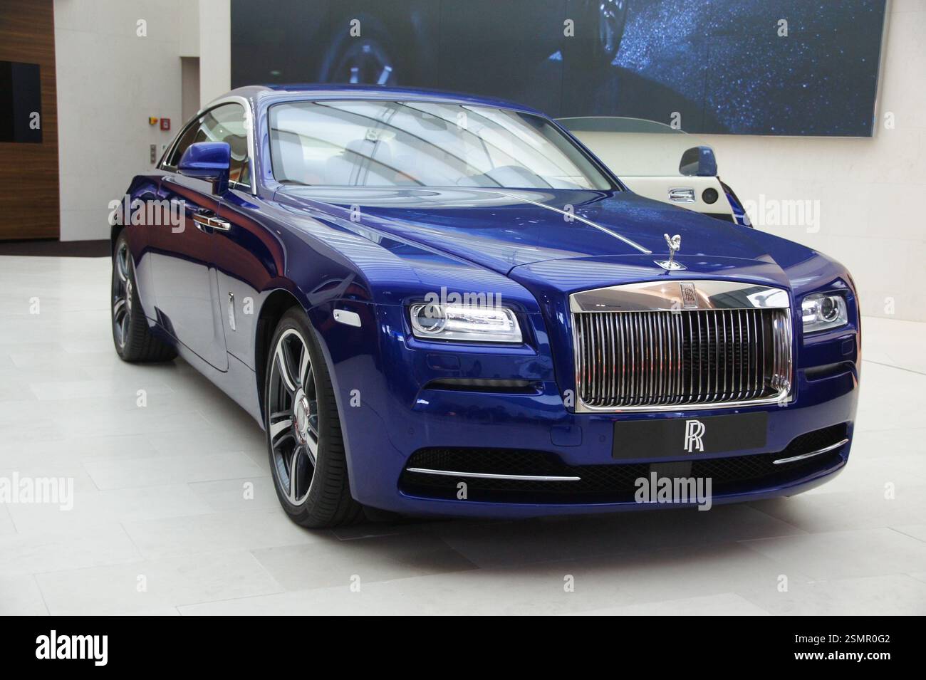 Deutschland, München. Ein luxuriöser blauer Rolls-Royce Wraith sitzt stolz in einem Showroom. Das schlanke, moderne Design deutet auf den versteckten Hochleistungsmotor hin Stockfoto