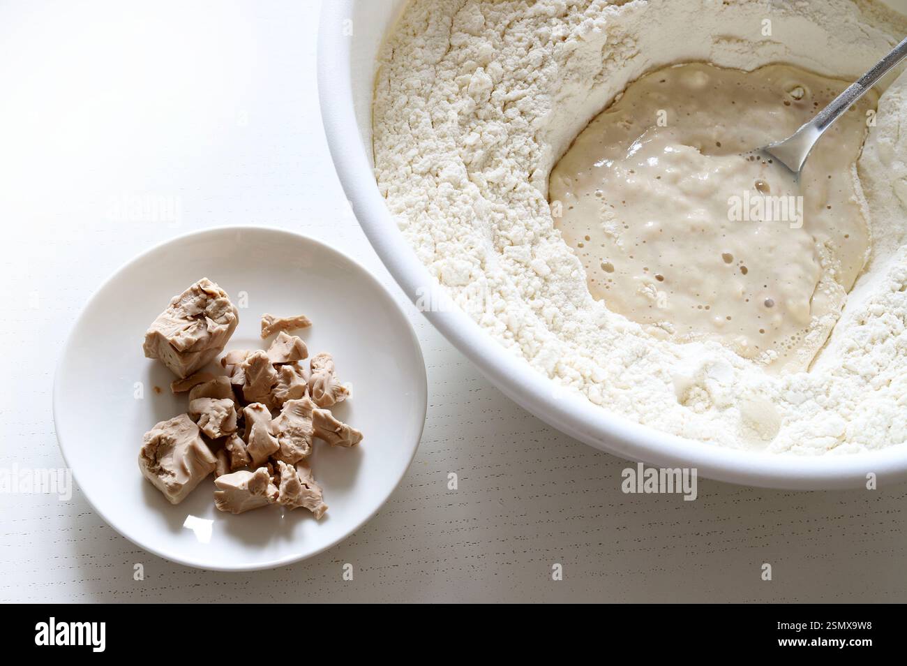 In Mehl gelöste frische Bierhefe für die Zubereitung von Pizzateig, Brot in einer Schüssel und frische Bierhefe auf einem Teller auf weißem Hintergrund. Stockfoto
